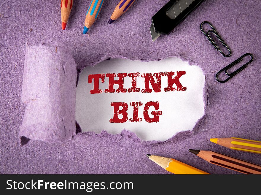 THINK BIG concept. Text under torn paper. Pencils and office supplies on an paper background