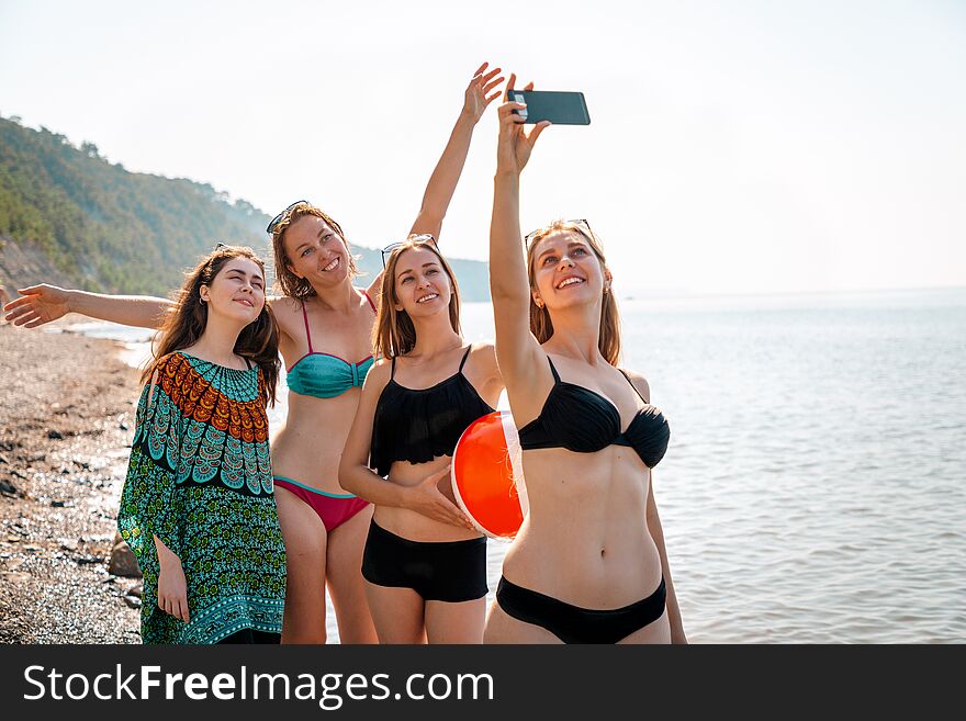 A group of young caucasian women take selfies on the beach. In the background-the sea and sky. Copy space. Concept of sea holidays and technologies.