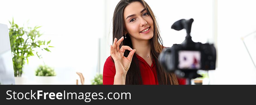 Portrait of beautiful smiling woman recording video-blog on video camera. Cheerful blogger showing ok sign with fingers. Blogging and creation concept. Portrait of beautiful smiling woman recording video-blog on video camera. Cheerful blogger showing ok sign with fingers. Blogging and creation concept