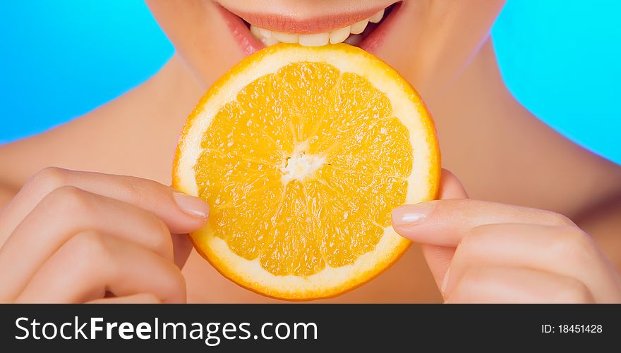 Woman with relish eating a slice of orange on a blue background