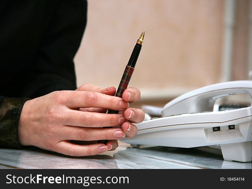 Women's hand holding pen near the phone. Women's hand holding pen near the phone