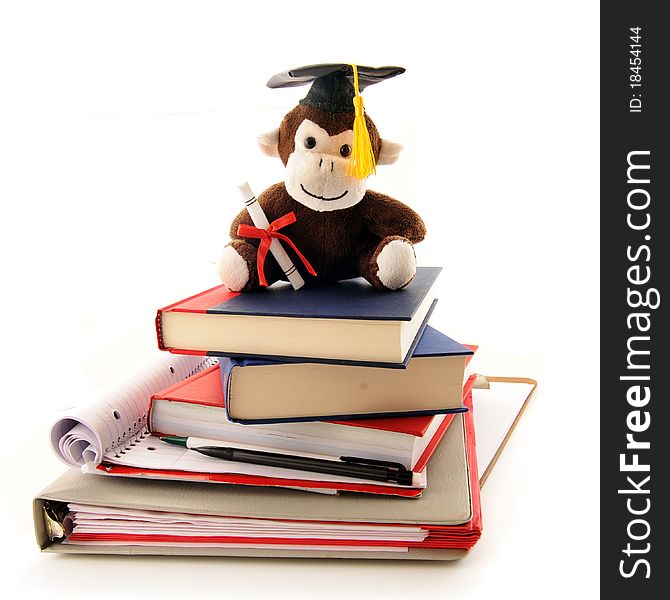 A stuffed monkey with a graduation cap and diploma sitting on top of a pile of used notebooks and texts.  Isolated on white. A stuffed monkey with a graduation cap and diploma sitting on top of a pile of used notebooks and texts.  Isolated on white.