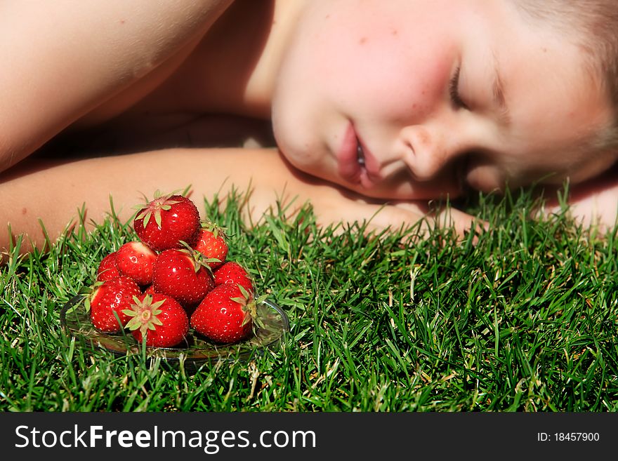 Boy sleeping on grass with pile of ripe strawberries in foreground. Boy sleeping on grass with pile of ripe strawberries in foreground.