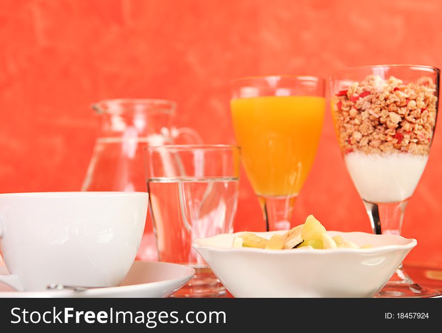 A healthy breakfast consisting of a fruit salad, glass of juice, coffe, cereals, yogurt and a glass of water