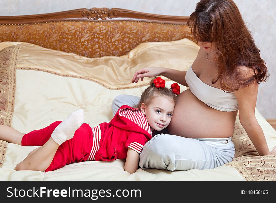 A smiling girl listens to the mother's abdomen. A smiling girl listens to the mother's abdomen