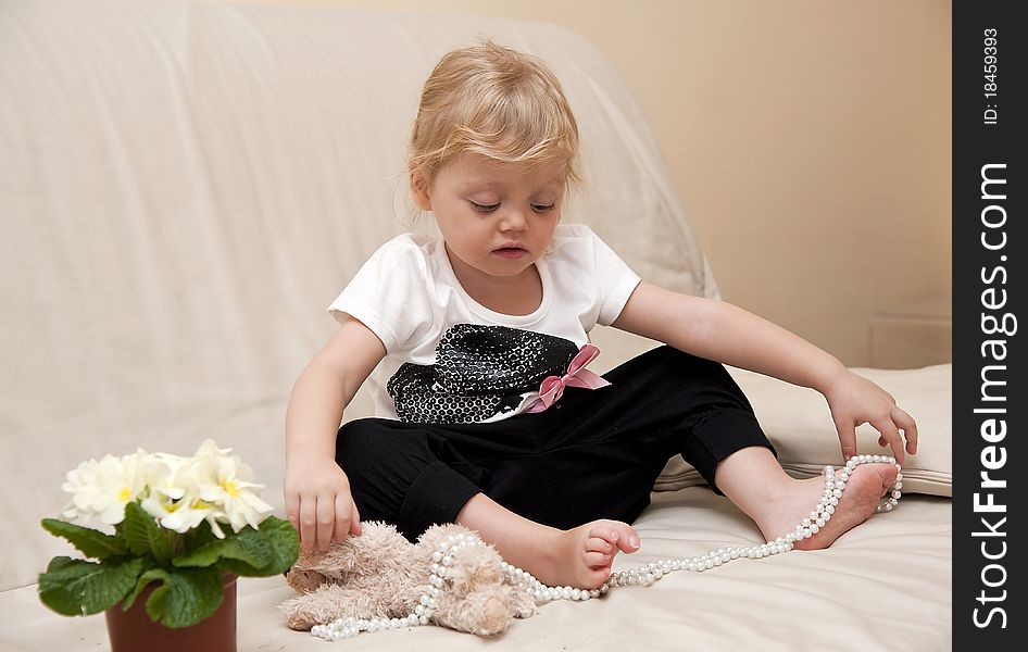 Girl sitting on a white sofa and playing with beads and toys. Girl sitting on a white sofa and playing with beads and toys