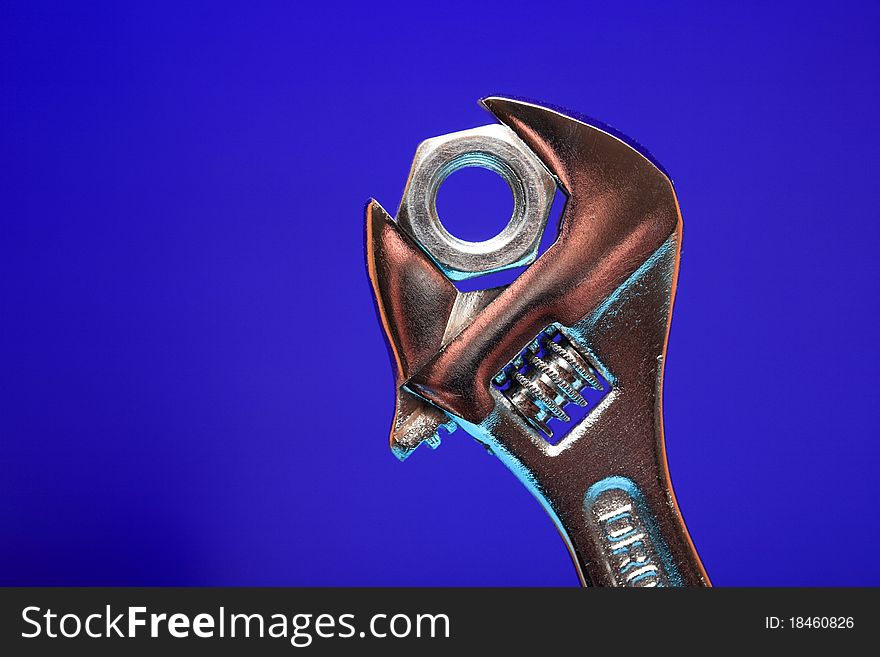 Extreme closeup of adjustable wrench gripping a nut on blue background. Extreme closeup of adjustable wrench gripping a nut on blue background