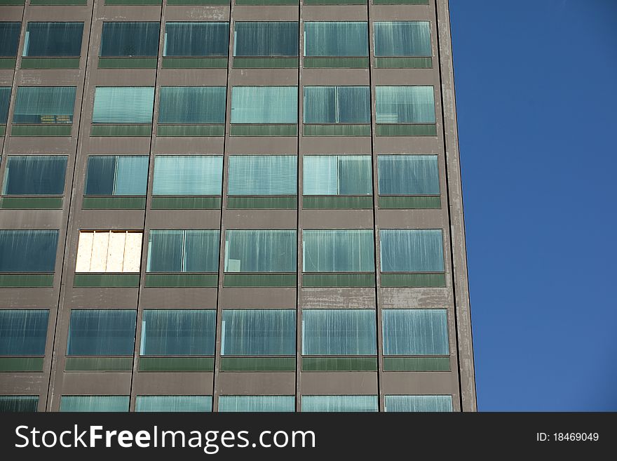 Looking up at a dirty office building with a boarded up missing window. Looking up at a dirty office building with a boarded up missing window