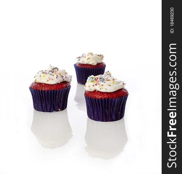 Three mini cupcakes with sprinkles on a white reflective set.
