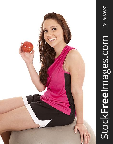 A woman is sitting on a body ball holding an apple smiling. A woman is sitting on a body ball holding an apple smiling.