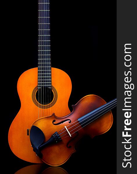 A close study of shapes and elements of design - vintage violin and wooden guitar side by side on dark backdrop. A close study of shapes and elements of design - vintage violin and wooden guitar side by side on dark backdrop.