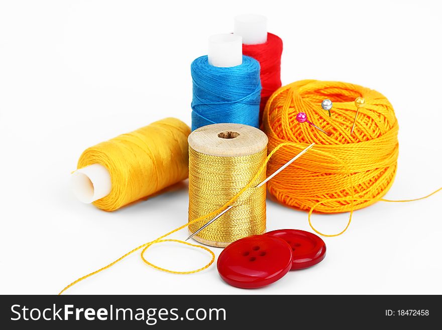 Colored thread, needles and buttons on a white background