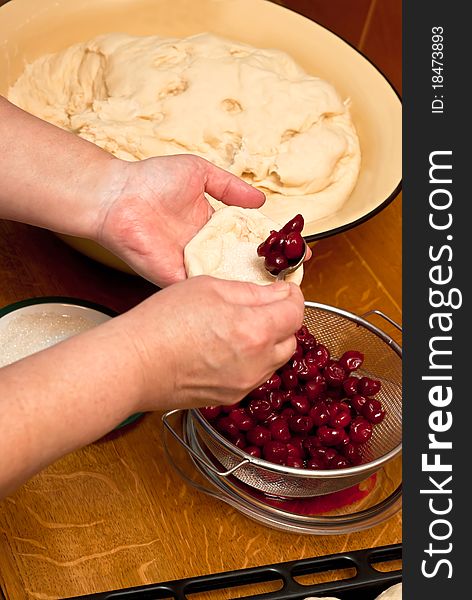 Female hands making small pies with cherry on a table. Female hands making small pies with cherry on a table