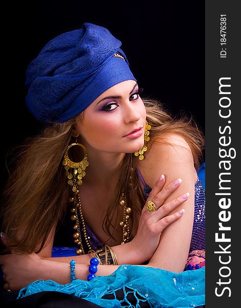 Beautiful girl in a turban and a stylized ethnic costume lies on headscarves