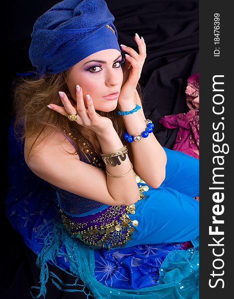 Beautiful girl in a turban and a stylized ethnic costume sits on headscarves