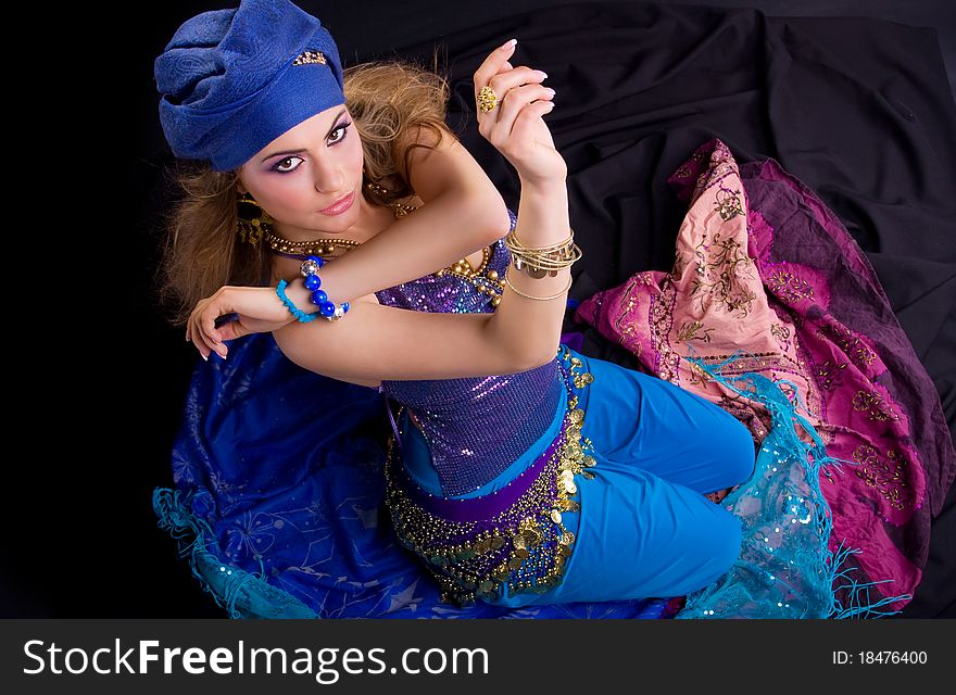 Beautiful girl in a turban and a stylized ethnic costume sits on headscarves