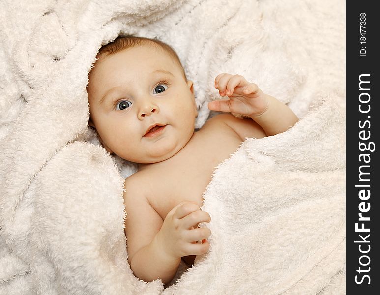 The baby lies in a white towel. He smiles. The baby lies in a white towel. He smiles