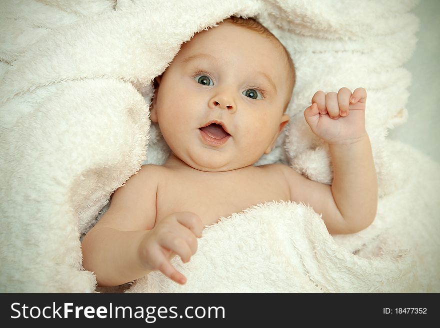 The baby lies in a white towel. He smiles. The baby lies in a white towel. He smiles