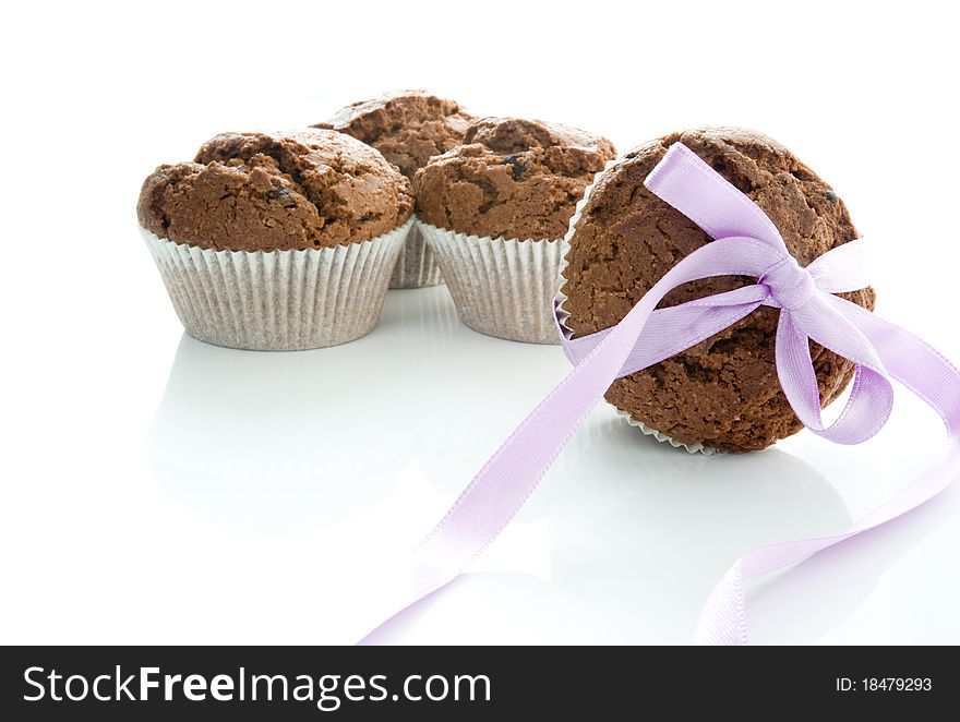 Four chocolate muffins on a white ground, one tied with a purple bow