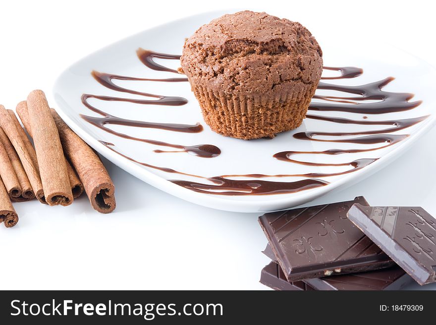 Chocolate muffin on a white plate decorated with chocolate, cinnamon sticks and a chocolate