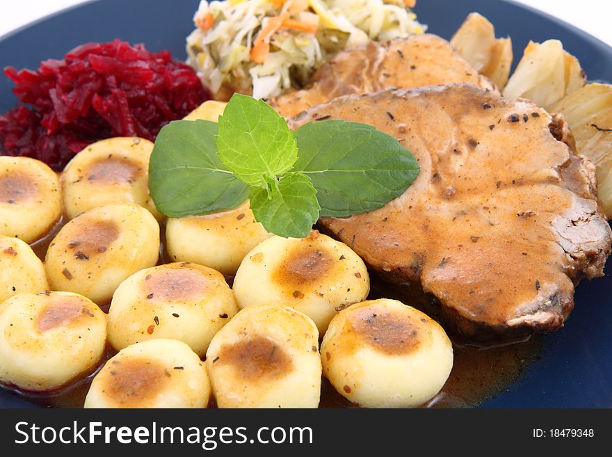 Pork steak and dumplings with side salads and baked onions, decorated with a mint twig, on a white background