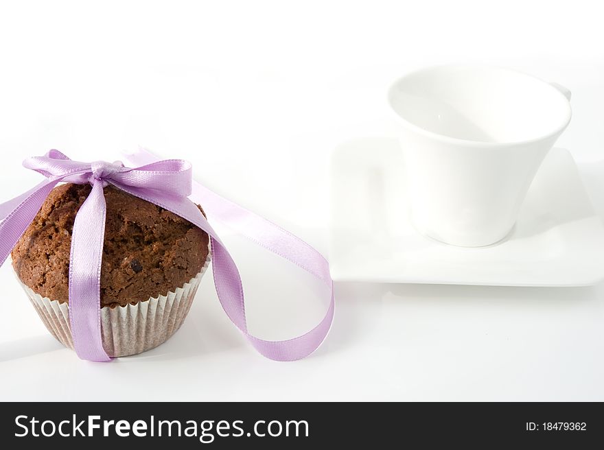 Chocolate muffin, tied with purple ribbon, with a white cup on a white background. Chocolate muffin, tied with purple ribbon, with a white cup on a white background