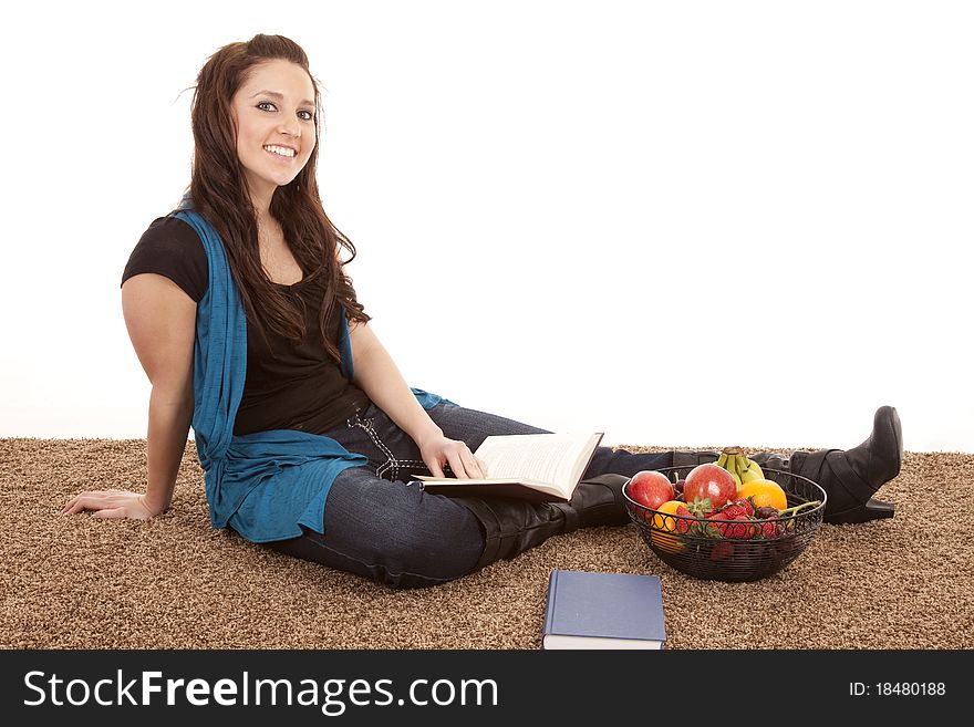 A woman is sitting by some fruit with a book. A woman is sitting by some fruit with a book.