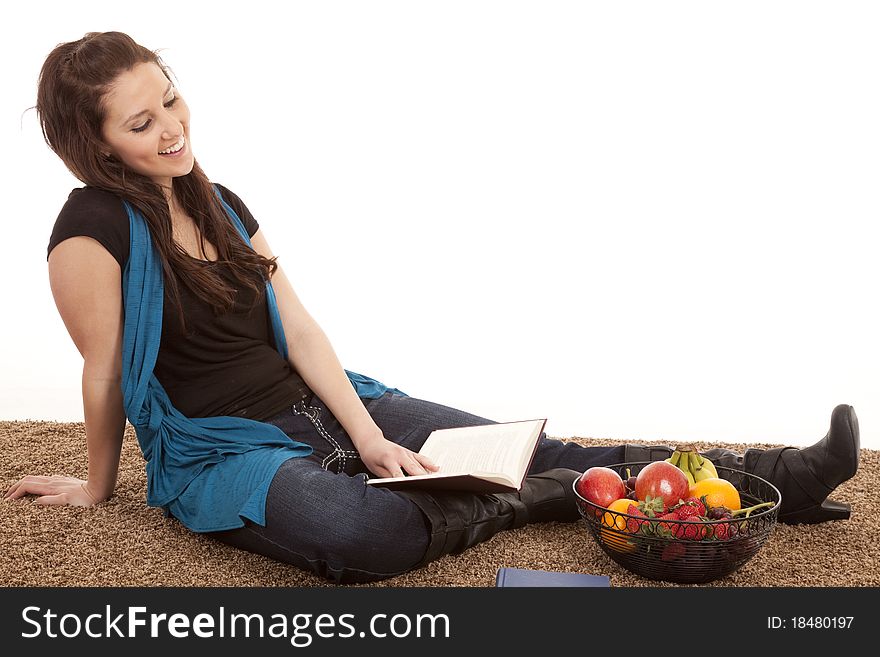 A woman is sitting on the floor reading by some fruit. A woman is sitting on the floor reading by some fruit.