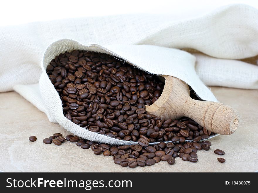 Coffee beans spilling out of a cream colored burlap sack.  Coffee scoop inside sack. Coffee beans spilling out of a cream colored burlap sack.  Coffee scoop inside sack.