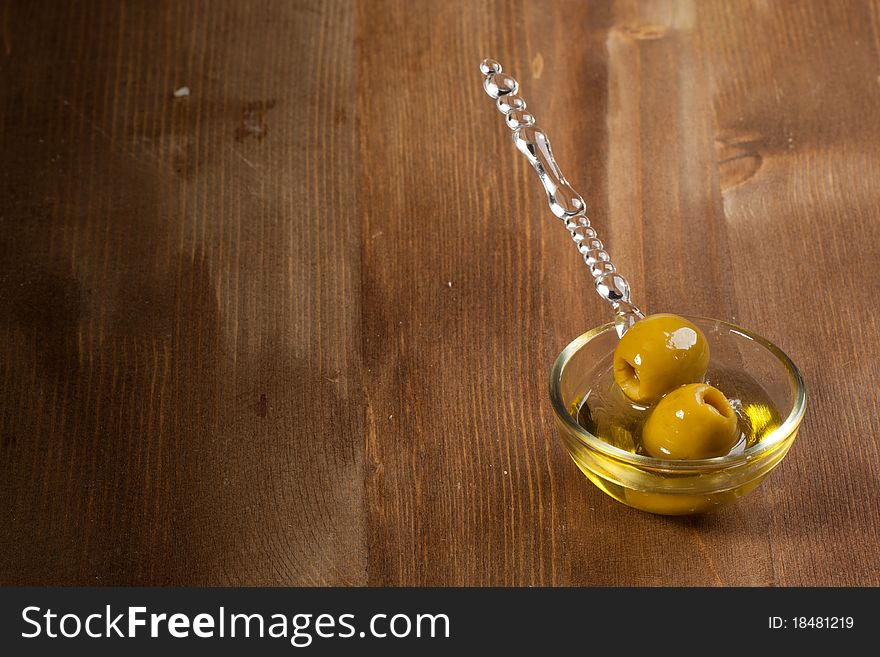 Snacks with green olives in little glass bowl on wooden background