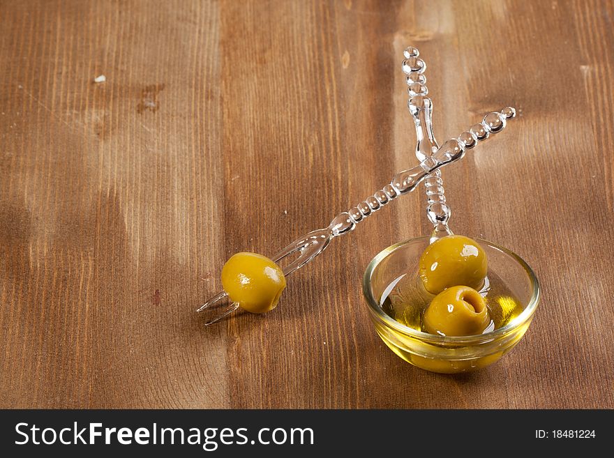 Snacks with green olives in little glass bowl on wooden background