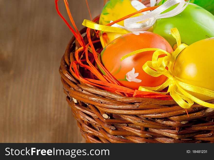 Colorful Easter eggs in basket on wooden background
