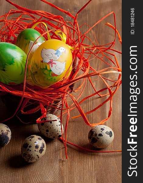 Colorful Easter and quail's eggs in orange nest on wooden table. Colorful Easter and quail's eggs in orange nest on wooden table