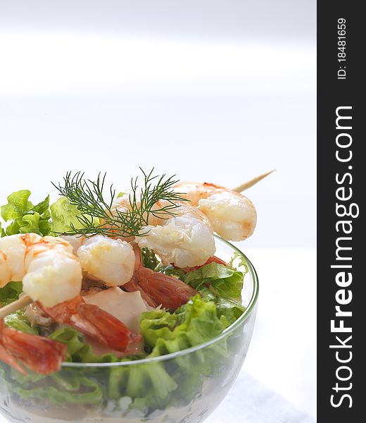 A prawn salad with lettuce,cucumber and dill in a bowl and a shrimp souvlaki on it. A prawn salad with lettuce,cucumber and dill in a bowl and a shrimp souvlaki on it