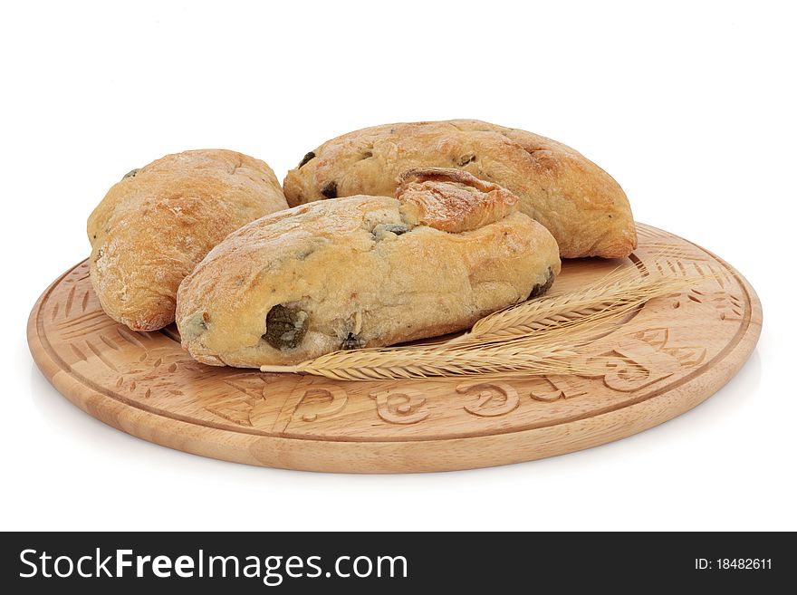 Olive bread roll selection on a carved wooden board with ears of wheat, over white background. Olive bread roll selection on a carved wooden board with ears of wheat, over white background.