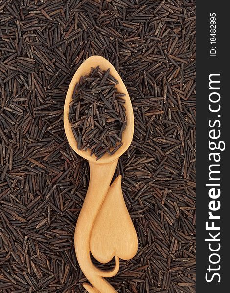 Wild rice in a carved wooden spoon with heart shape and forming a background.