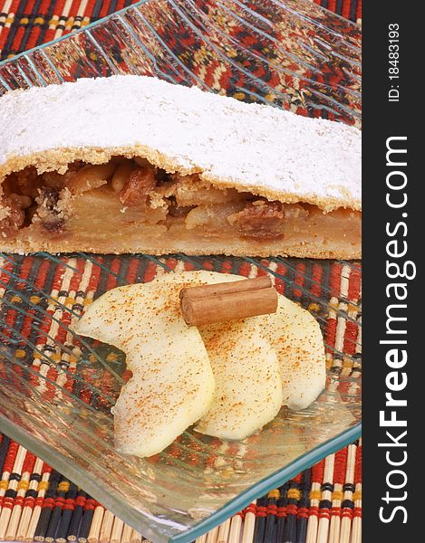 A slice of apple strudel served on a glass plate with apple slices and cinnamon. A slice of apple strudel served on a glass plate with apple slices and cinnamon