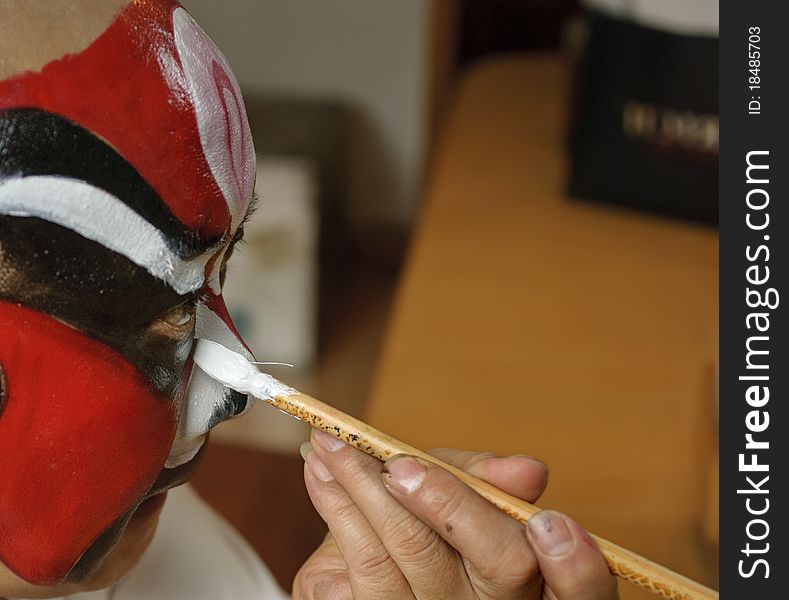 A chinese opera actor is painting his face backstage.