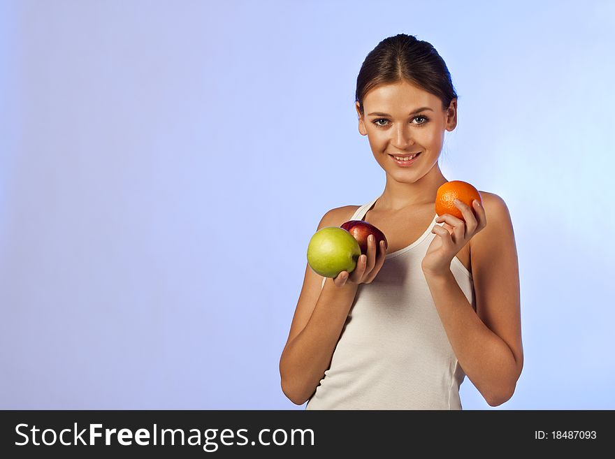 Young beautiful brunette is holding fruit on blue background isolated