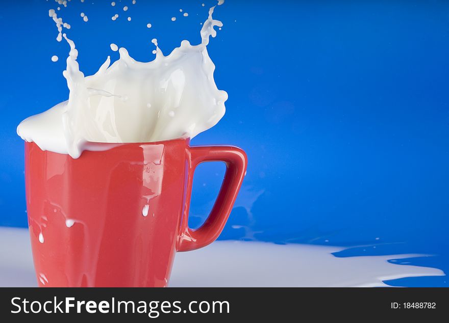 Milk splashing out of red cup over blue background. Milk splashing out of red cup over blue background