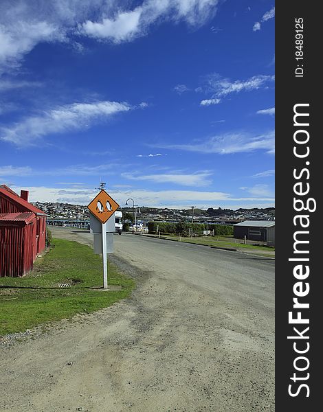 Road to the Oamaru Penguin colony - iconic kiwi attraction. Famous sign on the side of the road warning visitors about crossing penguins. Road to the Oamaru Penguin colony - iconic kiwi attraction. Famous sign on the side of the road warning visitors about crossing penguins.