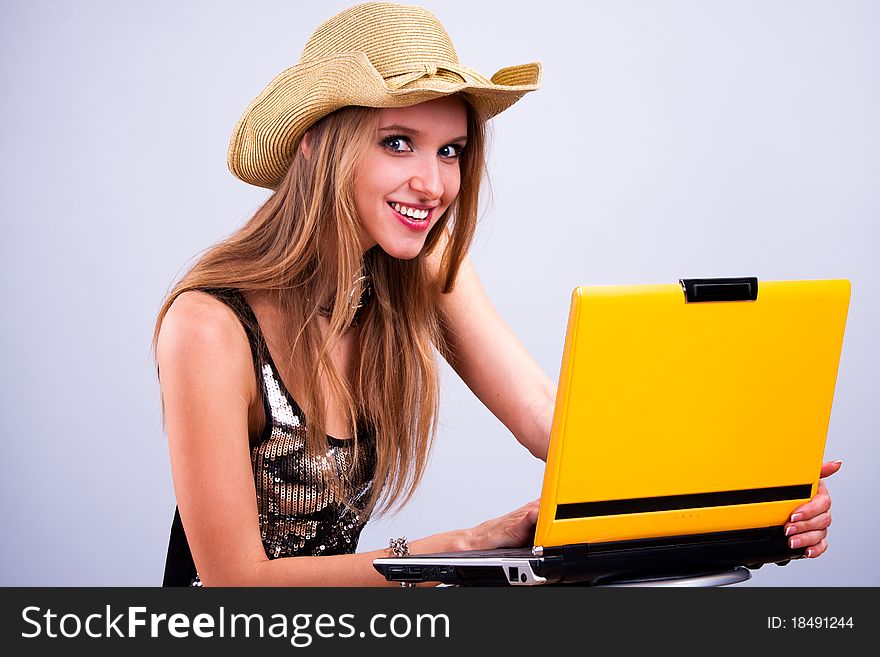 Attractive girl in a straw hat wth a yellow laptop