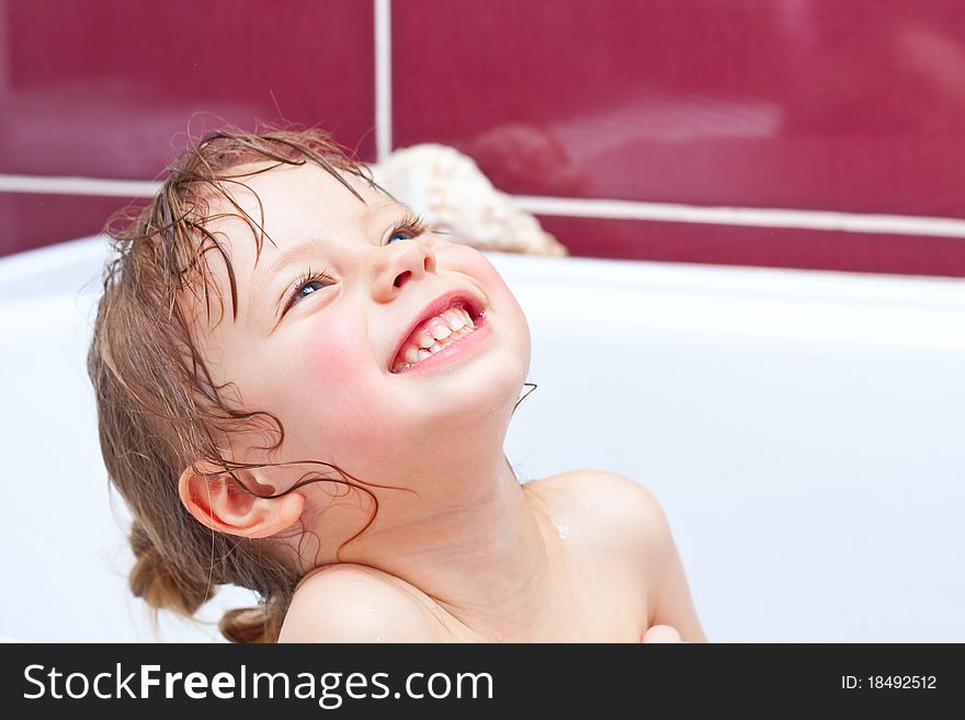 Cute three-year-old girl looking out of a bath and smiling
