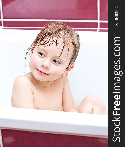 Cute three-year-old girl looking out of a bath and smiling