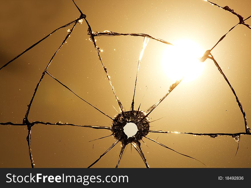 Hole and cracks in transparent glass after a shot against the sun. Hole and cracks in transparent glass after a shot against the sun