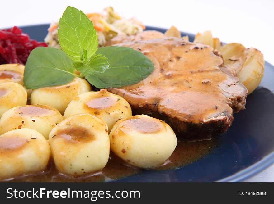 Pork steak and dumplings with side salads and baked onions, decorated with a mint twig, on a white background