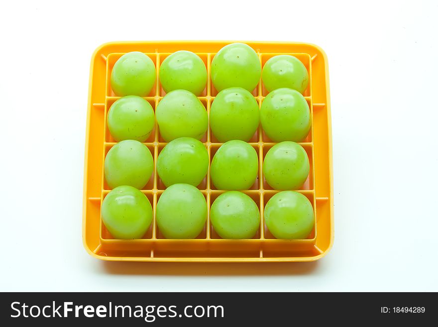 Sixteen green grapes in a square orange plastic holder set against a white background.