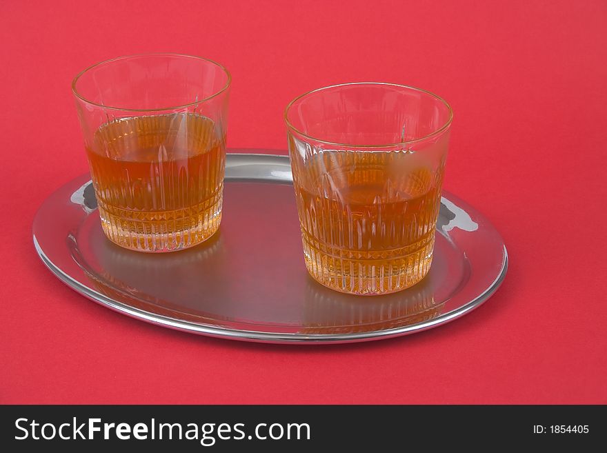 Two glasses with whiskey standing on a silver tray on red backgorund. Two glasses with whiskey standing on a silver tray on red backgorund