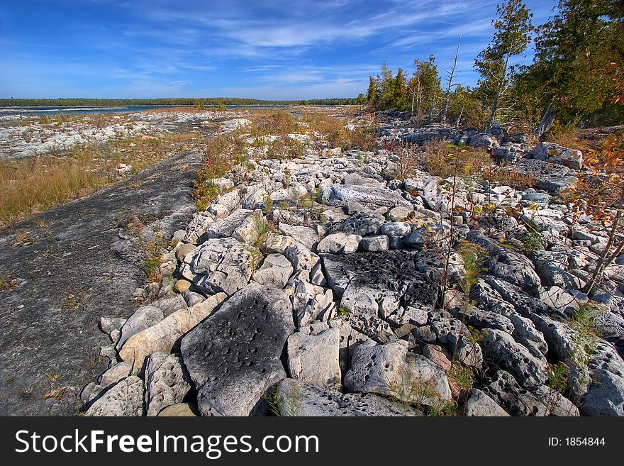 Meager vegetation finds its way through rocks and stones on a lake shore. Meager vegetation finds its way through rocks and stones on a lake shore.