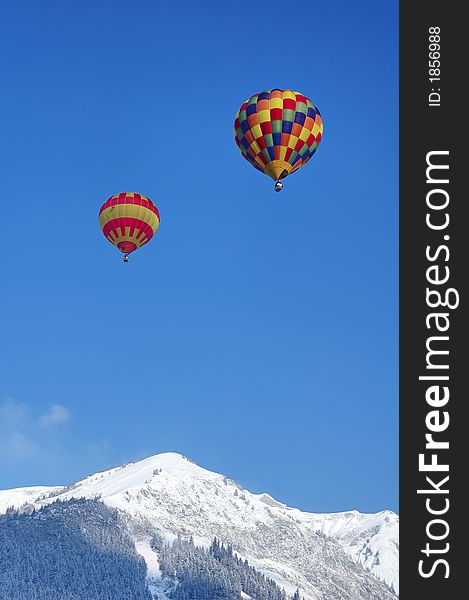 Two hot-air balloons rising over a snowy ridge in Switzerland. Two hot-air balloons rising over a snowy ridge in Switzerland.